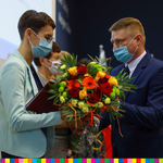 Członek zarządu województwa podlaskiego Marek Malinowski przekazujący kobiecie bukiet kwiatów. 