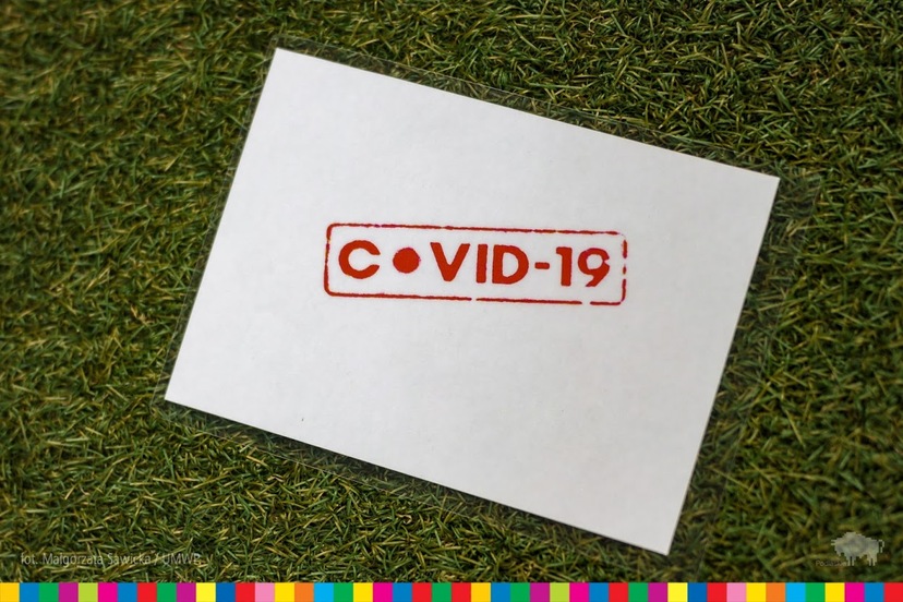 Biała karta na zielonym tle z czerwonym napisem COVID-19