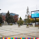 Plac miejski w Łapach z pomnikiem i telebimem oraz przechdzającymi się ludźmi