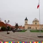 Maszt z flagą biało-czerwoną na Rynku w Tykocinie. Na drugim planie Kościół parafialny pod wezwaniem Trójcy Przenajświętszej w Tykocinie.