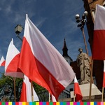 Flagi biało-czerwone na tle kościoła oraz pomnika.