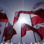 Na tle wschodzącego słońca powiewające flagi biało-czerwone.