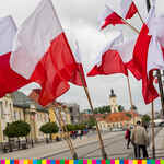 Na tle placu miejskiego powiewające flagi biało-czerwone.