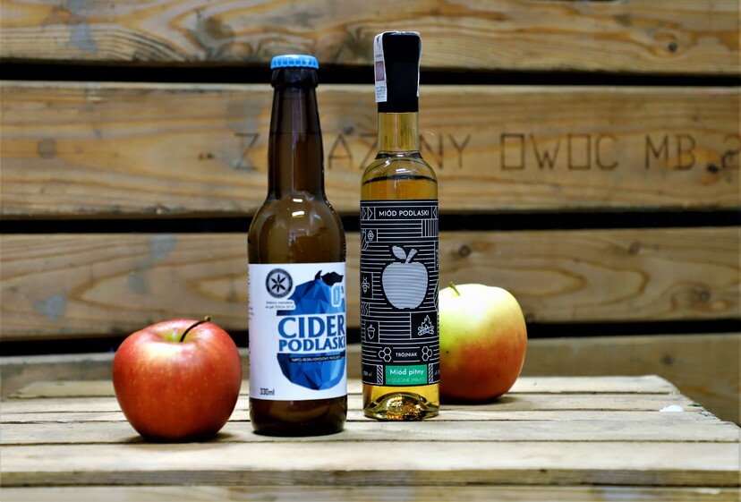 Cider i miód w butelkach na skrzyni drewnianej z jabłkami.