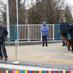 Na chodniku przed biało-niebieską barierką w tle stoi 5 osób wraz z psem