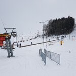 Wyciąg narciarski na stoku pokrytym śniegiem. Na drugim planie drzewa.