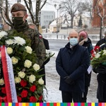 Na pierwszym planie żołnierz trzymający wieniec z biało-czerwonymi wstęgami. Za nim widoczny marszałek Artur Kosicki oraz wojewoda Bohdan Paszkowski trzymający kwiaty. Za nimi widoczna kobieta