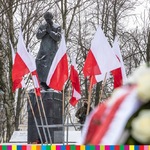 Między biało-czerwonymi powiewającymi flagami widoczny pomnik bł. ks. Jerzego Popiełuszki. Obok monumentu stoi dwóch żołnierzy Wojsk Obrony Terytorialnej