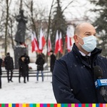 Marszałek Artur Kosicki udzielający wywiadu. W tle widoczna grupa osób stojąca pod pomnikiem bł. ks. Jerzego Popiełuszki