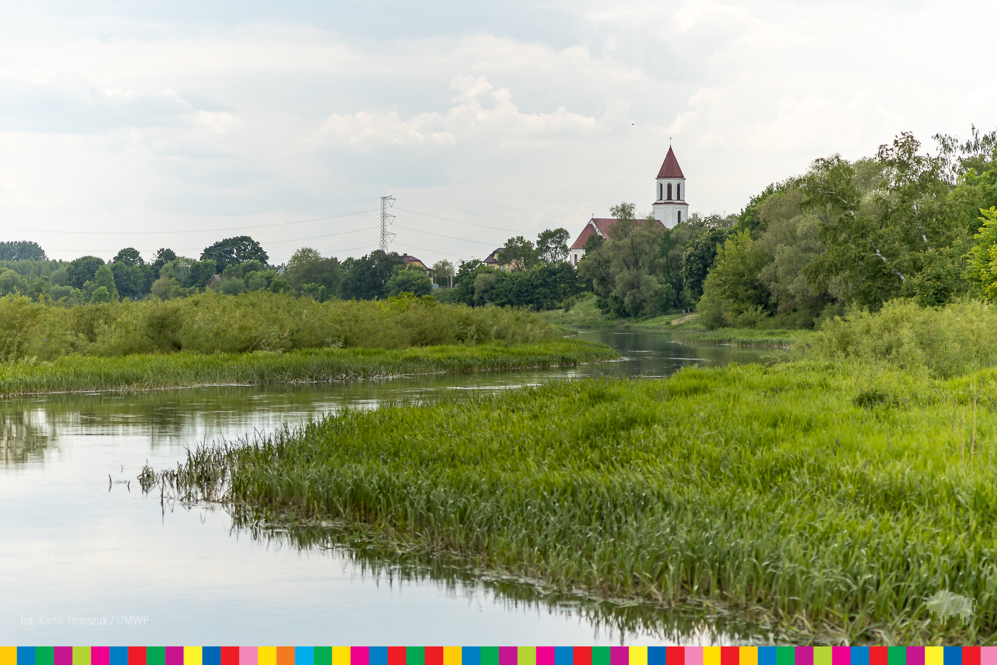 Rzeka i tereny zielone nad rzeką. W oddali wiczoczne są wieże kościoła