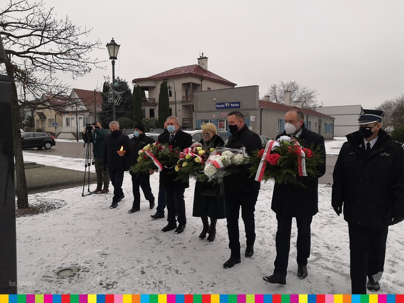 Grupa osób stoi z wiązankami kwiatów. W środku Wiesława Burnos, Członek Zarządu Województwa Podlaskiego.