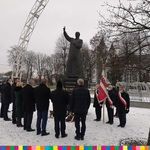 Grupa osób, w tym poczet sztandarowy stoją przy pomniku księdza Jerzego Popiełuszki