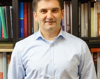 Zdjęcie doktora Piotra Guzowskiego na tle półek z książkami