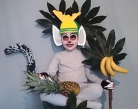 Dziecko przebrane za postać z bajki. Na kolanach leży ananas. Z prawej strony widzimy banany oraz liście.