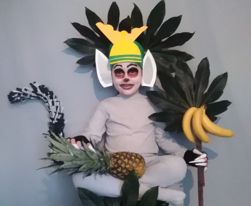 Dziecko przebrane za postać z bajki. Na kolanach leży ananas. Z prawej strony widzimy banany oraz liście.