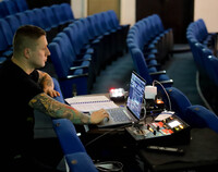 Mężczyzna siedzący na teatralnej widowni i pracujący przy laptopie i sprzęcie oświetleniowym