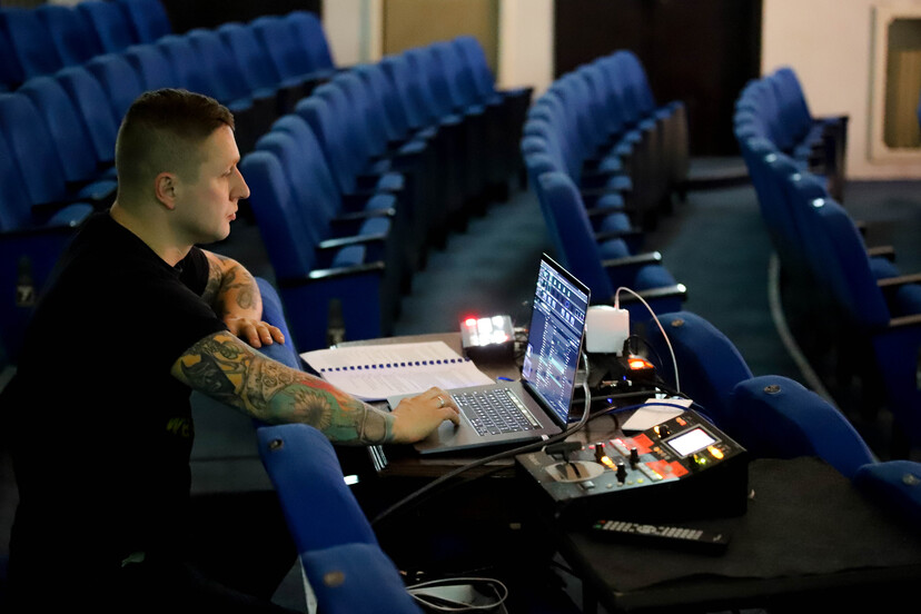 Mężczyzna siedzący na teatralnej widowni i pracujący przy laptopie i sprzęcie oświetleniowym