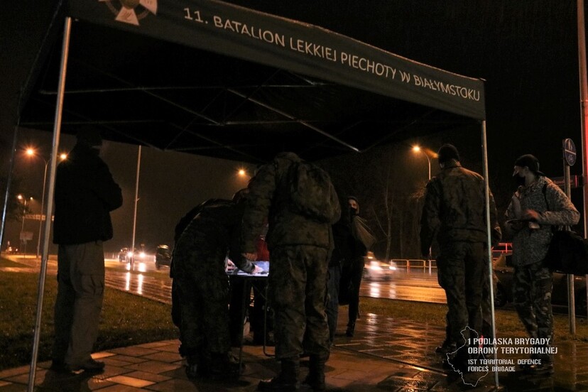 Grupa żółnierzy stoi pod namiotem z napisem 11 Batalion Lekkiej Piechoty w Białymstoku