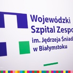 Logo szpitala: Biały krzyż na granatowo-zielonym tle. Obok napis: Wojewódzki Szpital Zespolony im. Jędrzeja Śniadeckiego w Białymstoku.