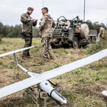 Zdjęcie drona. na drugim planie dwóch żołnierzy stoi przy pojeździe wojskowym.