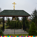 Dzwonnica uwieńczona złotym prawosławnym krzyżem. Na drugim planie rosną drzewa i krzewy.