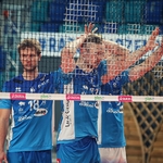 Trzech zawodników w niebieskich koszulkach których przysłania siatka