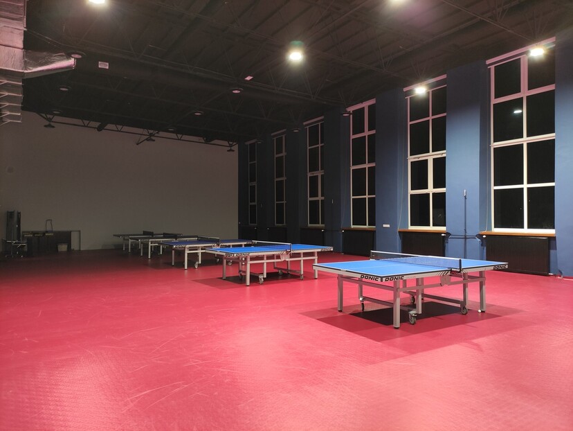 Odnowiona sala treningowa UKS Dojlidy z oświetleniem, czerwoną podłogą i niebieskimi stołami do gry