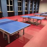 Oświetlona sala z czerwoną podłogą i niebieskimi stołami do tenisa