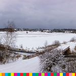Panorama krajobrazu Białowieży z zaśnieżonymi łąkami, rzeką oraz mostem