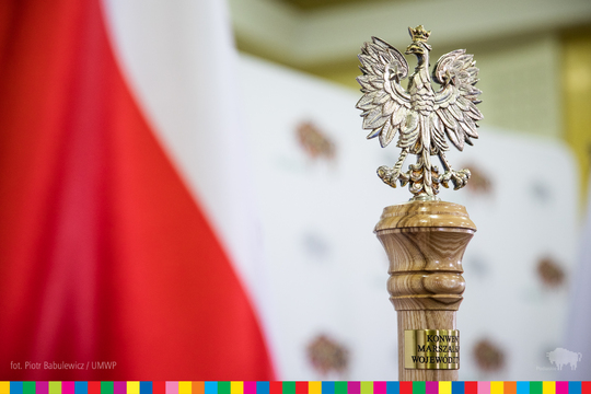 Laska marszałkowska zwieńczona figurą orła. Po lewej flaga Polski.