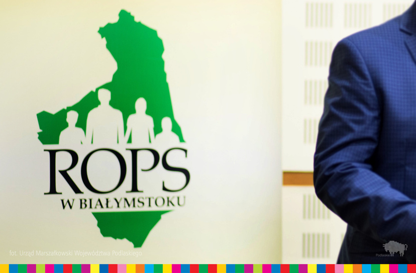 Po lewej logo ROPS w Białymstoku. Po prawej fragment ręki mężczyzny w garniturze.