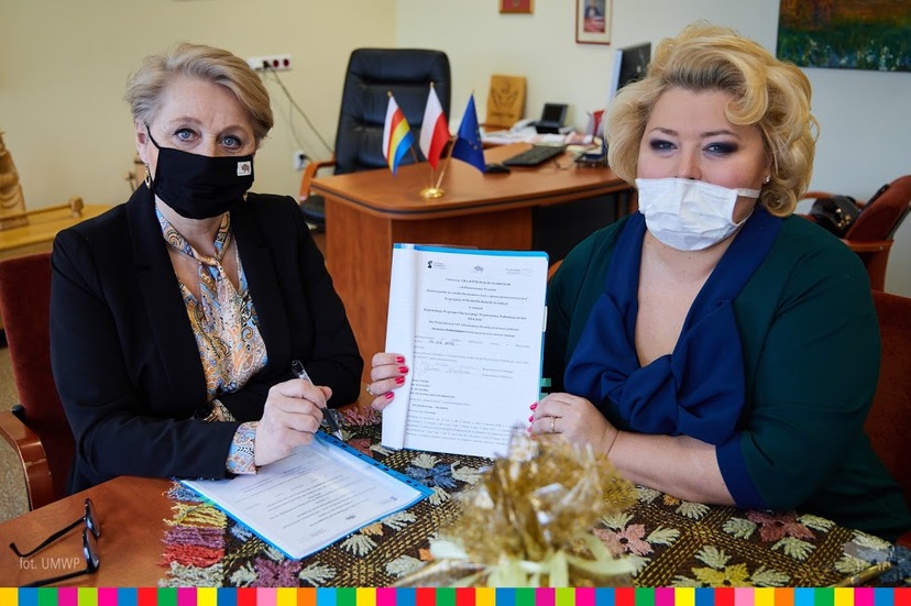 Przy stole siedzą: Wiesława Burnos i Ewa Kulikowska, która w ręku trzyma umowę