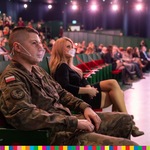Na widowni na pierwszym planie siedzi mężczyzna ubrany w mundur wojskowy.