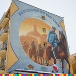 Zdjęcie muralu na ścianie budynku. Mural przedstawia ułana na koniu na tle innych ułanów i zabudowań.