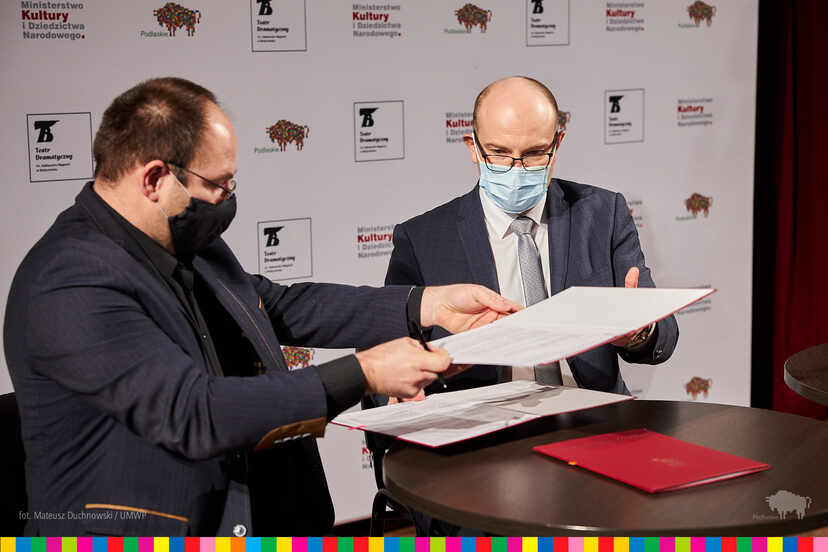 Marszałek Województwa Podlaskiego Artur Kosicki oraz Piotr Półtorak, dyrektor Teatru Dramatycznego w Białymstoku podają sobie teczkę z dokumentami do podpisu.