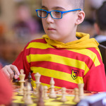 Chłopiec znad szachownicy patrzy na drugiego zawodnika