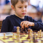 Chłopiec patrzy na szachownicę i zastanawia się nad ruchem pionkami