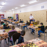 Kilkudziesięciu młodych chłopców i dziewcząt siedzi przy stolikach i gra w szachy