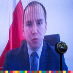 Adam Andruszkiewicz, sekretarz stanu w Kancelarii Prezesa Rady Ministrów. W tle widoczna biało-czerwona flaga Polski.
