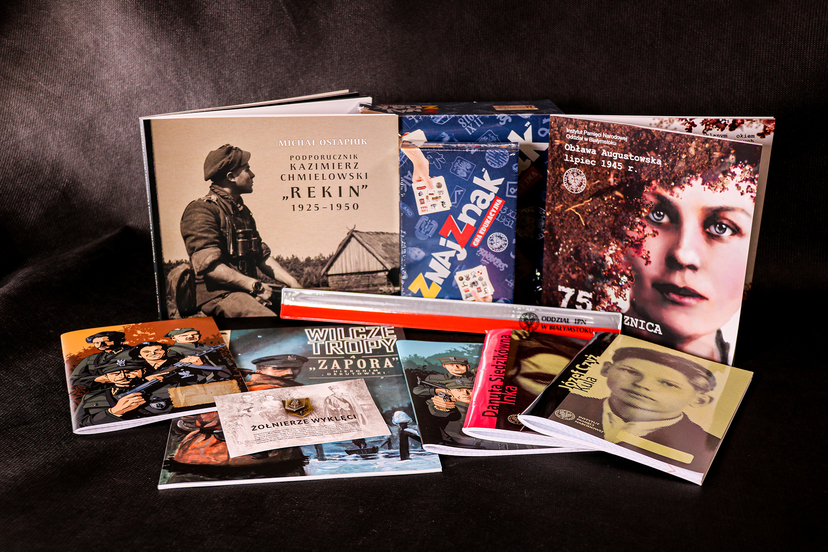 Zeszyty, broszury z wizerunkami Żołnierzy Niezłomnych ułożone na stole.