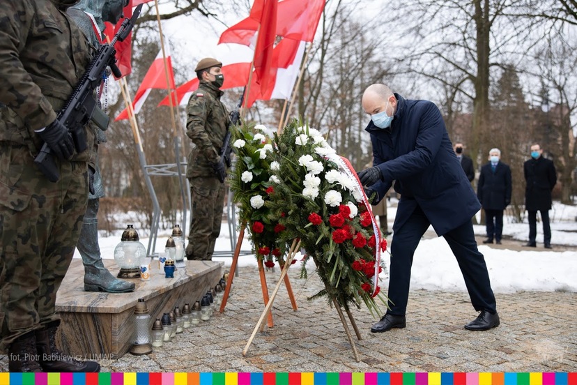 Marszałek Artur Kosicki składa wieniec z biało-czerwoną wstęgą przed pomnikiem. W tle flagi oraz żołnierz stojący na warcie