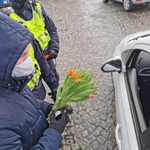 Mężczyzna wręcza kwiaty osobie siedzącej w samochodzie. Za nim stoją policjanci.