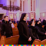 Na zdjęciu stoją osoby uczestniczące we mszy świętej. Z prawej strony widoczne siostry zakonne