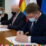 Trzy osoby. Po prawej Marek Malinowski w trakcie podpisywania umowy.