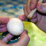 Dłonie trzymające batik szpilkowy oraz jajko z namalowanym wzorkiem