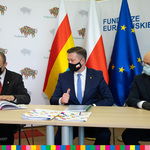 Wicestarosta białostocki Roman Czepe podpisuje umowę o dofinansowanie szkolnictwa zawodowego w okolicach Białegostoku. Od prawej siedzi dwóch męzczyzn. W tle widoczne trzy flagi