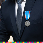 W klapie garnituru medal zamocowany na niebieskiej taśmie z biało-czerwonymi paskami.