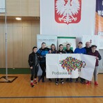 Dziewczyny wraz z trenerami trzymają w ręku baner z logotypem Województwa Podlaskiego