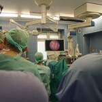 Kilkoro lekarzy w fartuchach lekarskich przygląda się operacji na ekranie monitora
