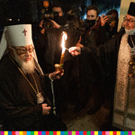 Ksiądz prawosławny zapala świecę abp Sawie. W tle widoczni operatorzy trzymający kamery